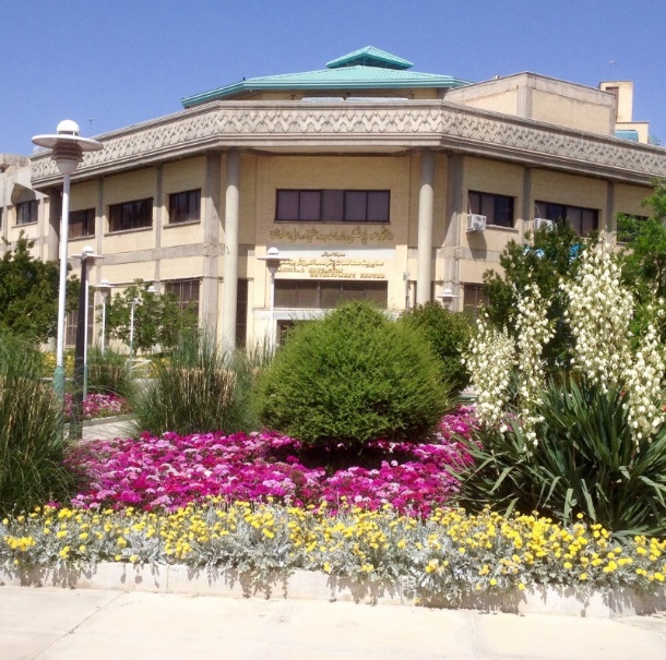 Das Gebäude der Medical Education: Ein sechseckiger Grundriss mit mehreren Stockwerken.  Der Dachfirst ist in iranisch-arabischer Ornamentik verziert, das Dach ist türkisblau, die Farbe Isfahans. Das Gebäude selbst ist hell gestrichen, es gibt nur kleine Fenster, als Schutz vor der Hitze. Im Garten vor dem Gebäude blühen üppig verschiedene Pflanzen, Gräser und Büsche.